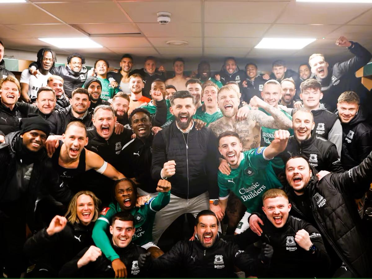 in a dressing room, celebrating footballer crowd together for a photograph.
