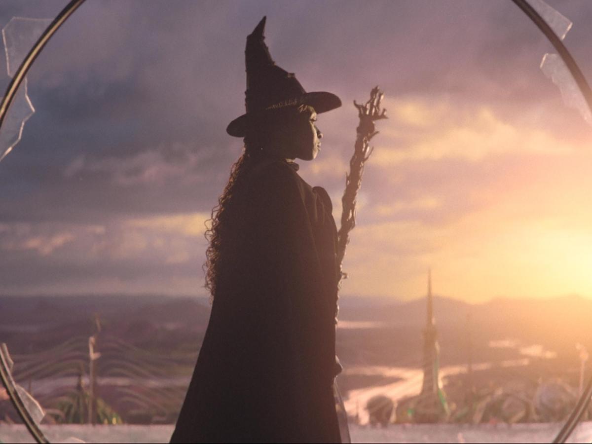 In a still from Wicked, the witch stands and looks to the sunset.