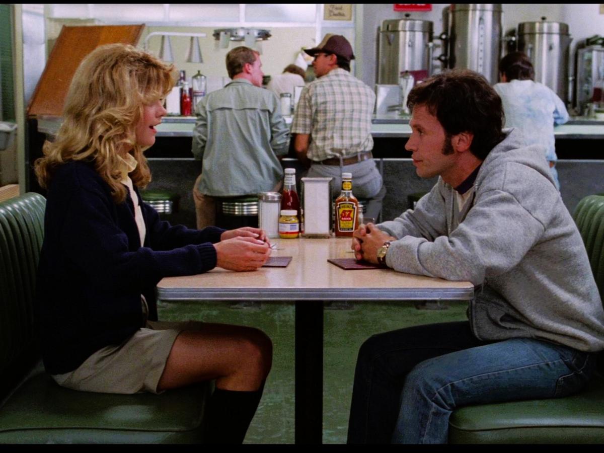 A couple sit at a table in a diner talking intensely.