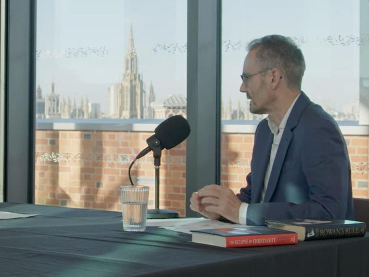 A podcast guest sits at a table in front of a mic. 