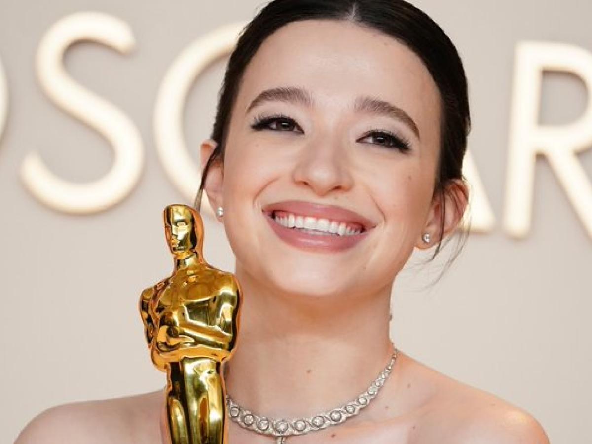 Mikey Madison, wearing a ball gown, clutches a golden Oscar statue.