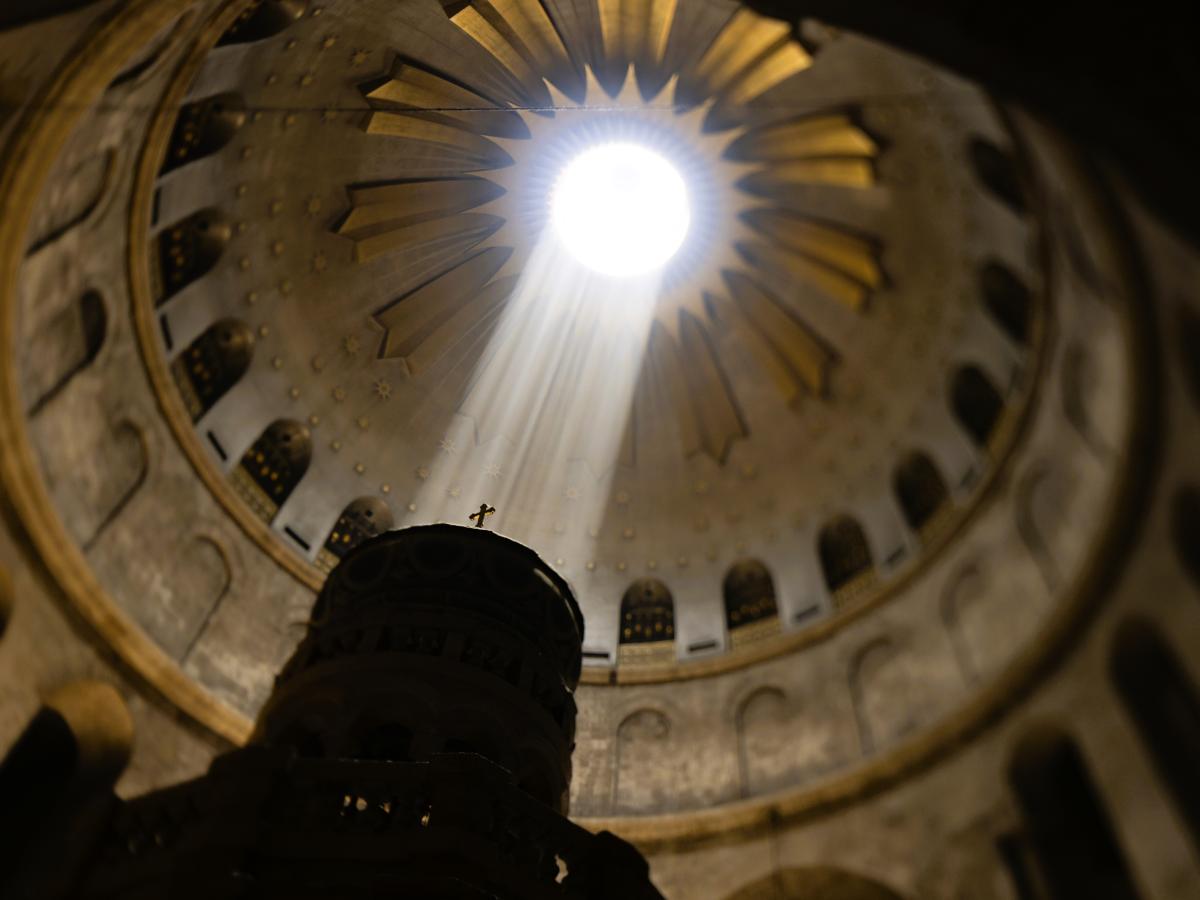 A shaft of light from an opening in a dome lights a cross on a pedestal.