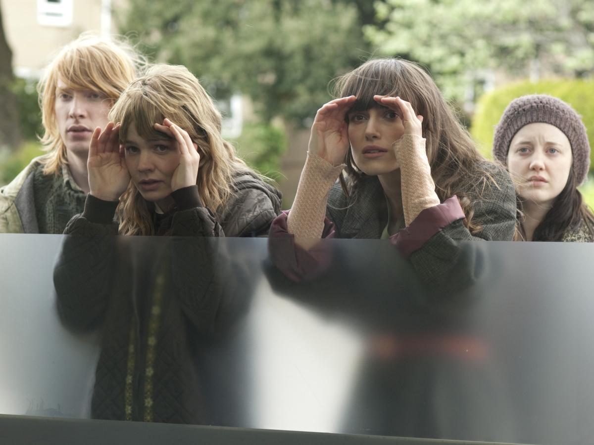 Four young people peer through a window.