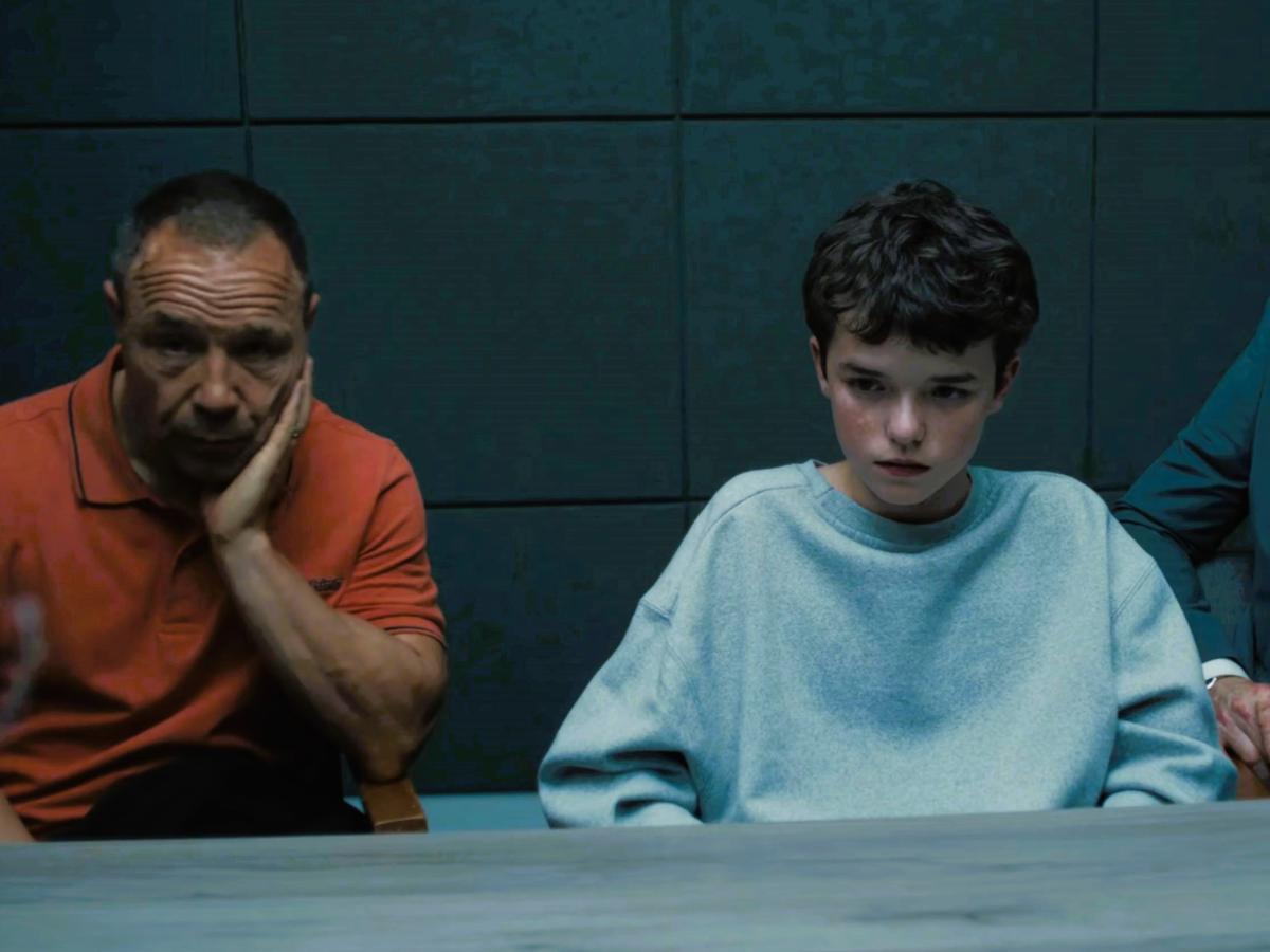 An unhappy father sits next to a scared son in a police interview room.