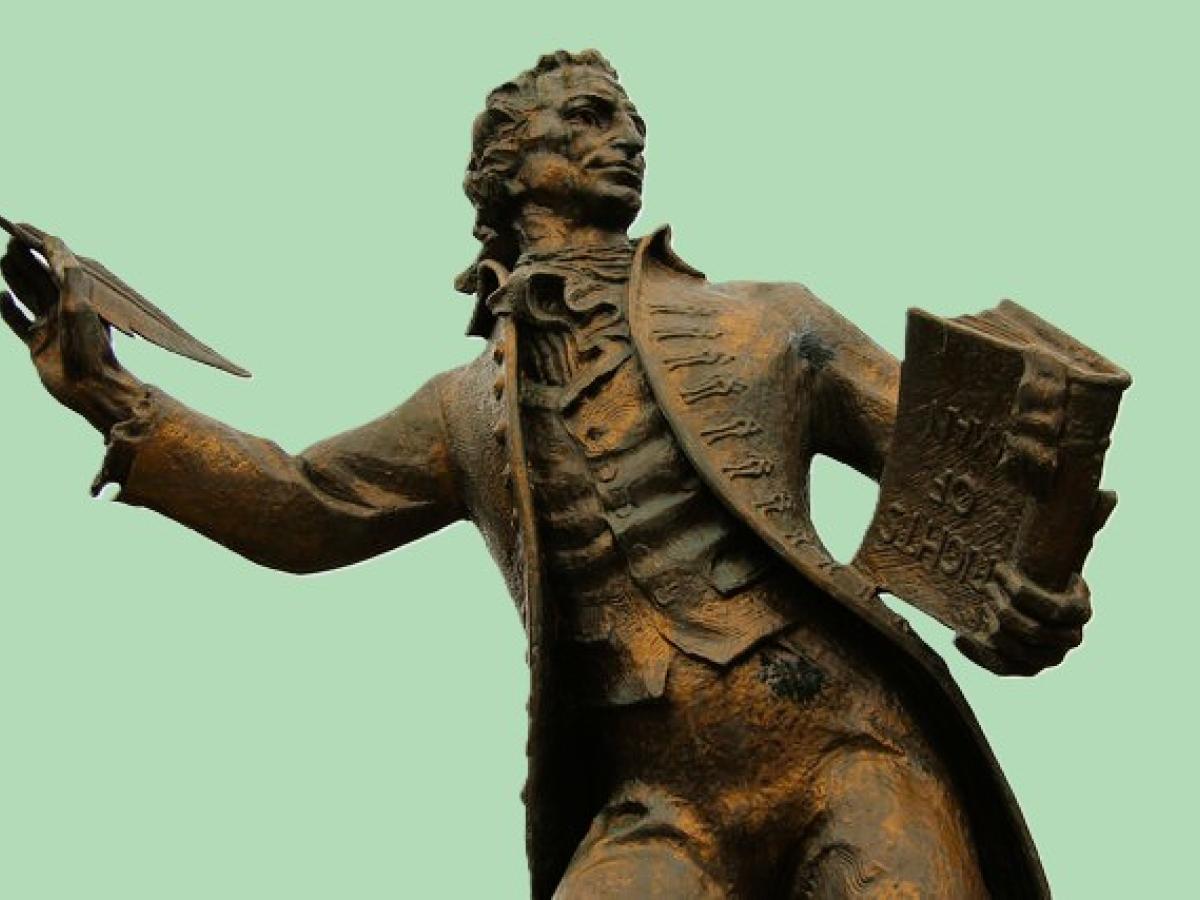A statue of a 18th century man holding a pen and a book.