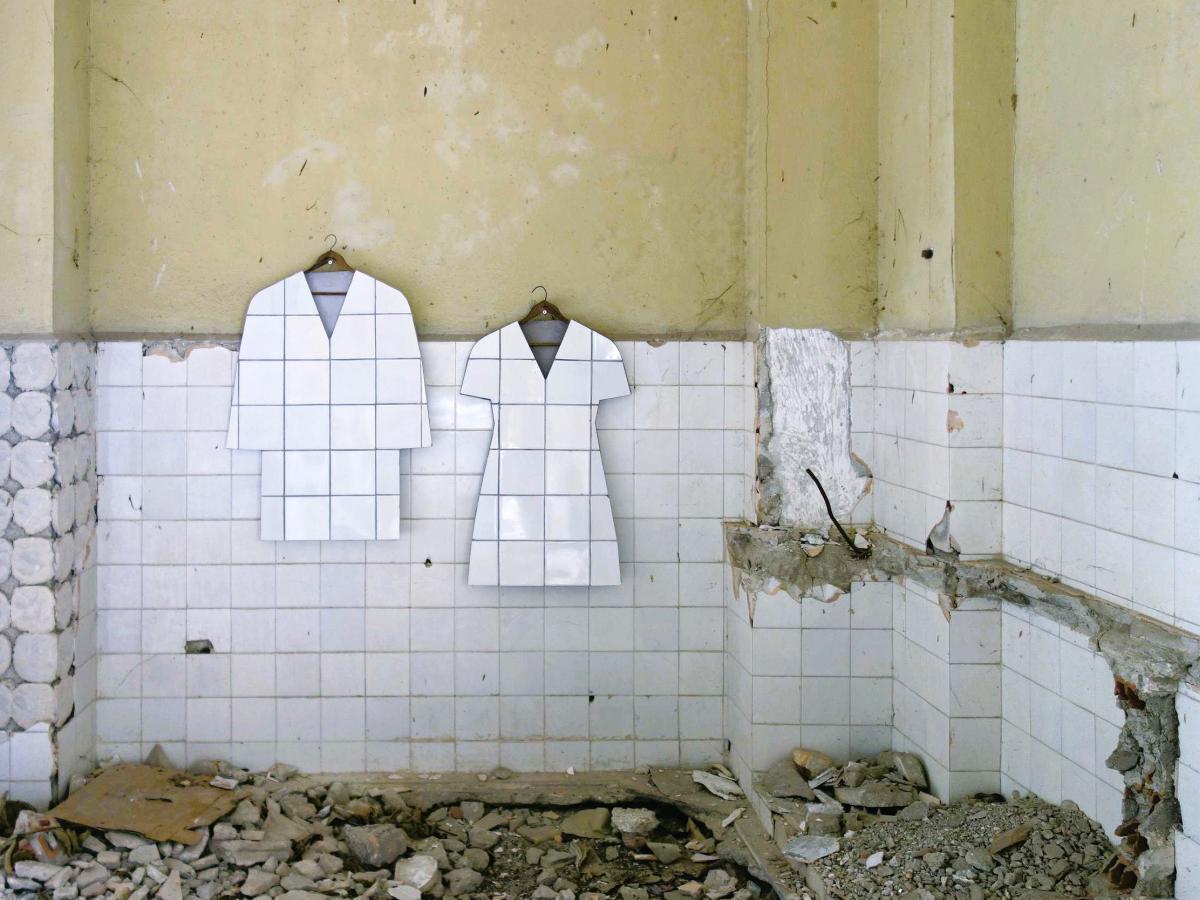 In a bombed-out tiled room, two art works hang in the shape of a tiled jacket and shape
