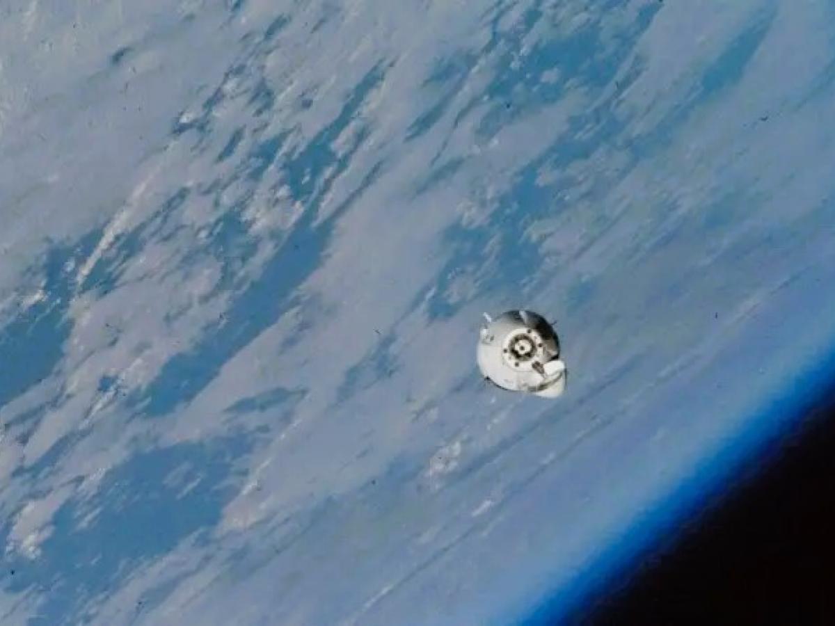 A small white space capsule orbits around the earth.