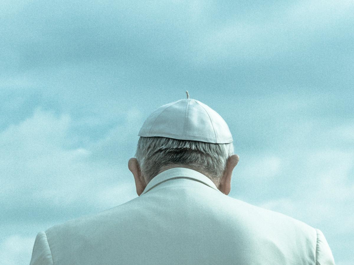 A pope wearing a white skull cap and white robe, viewed from behind