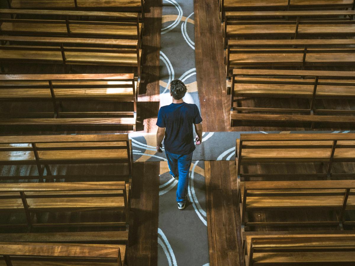 A casually dressed man strides down the aisle of a church between the pews.