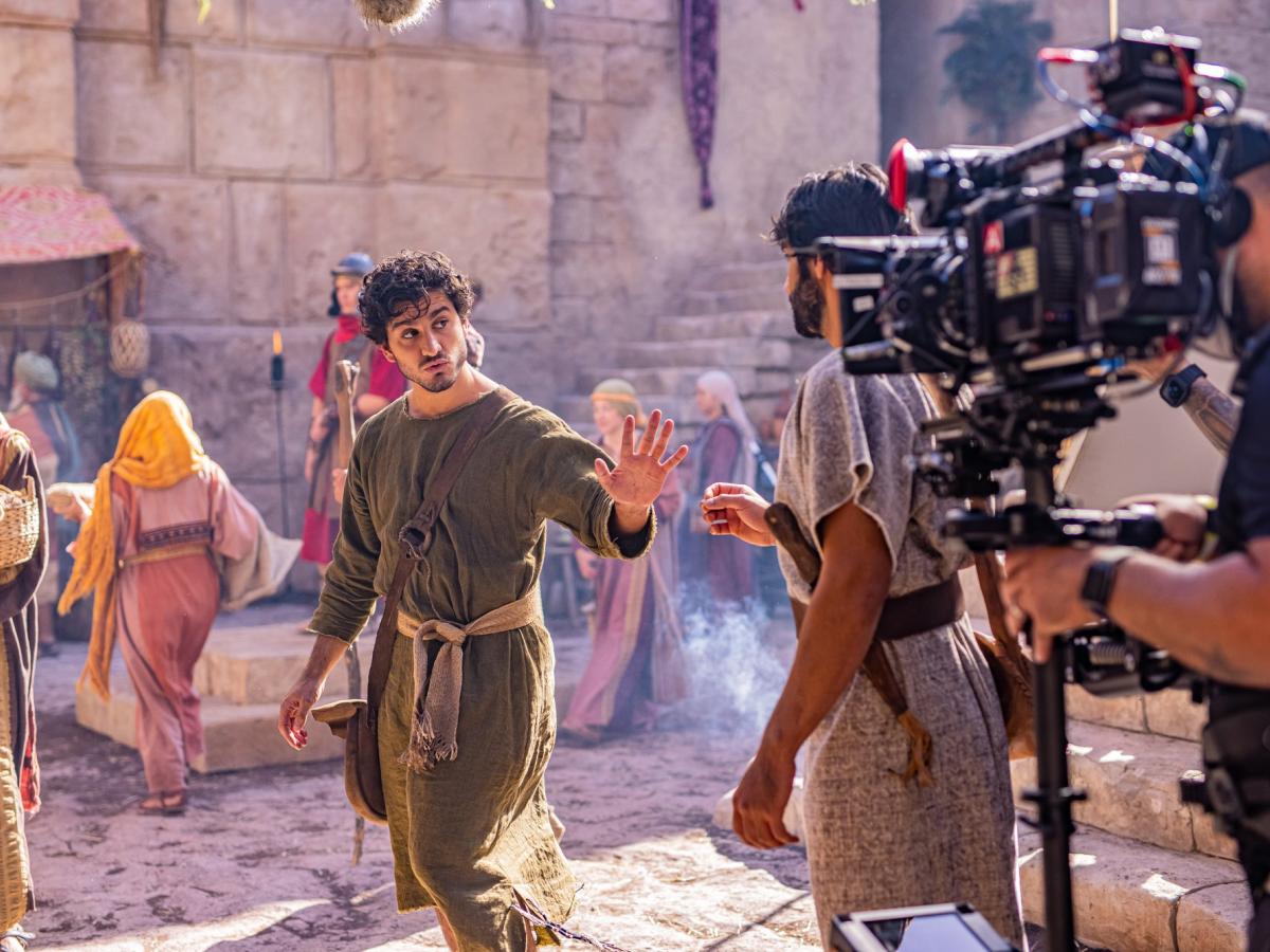 An actor dressed in an ancient Middle Eastern way is filmed by a large camera.