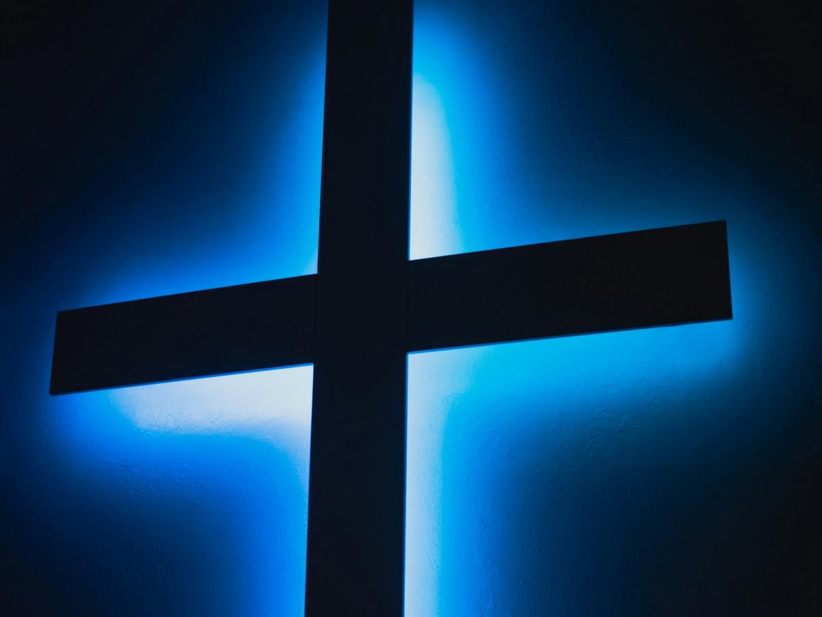 A black cross is backlit bya blue light.
