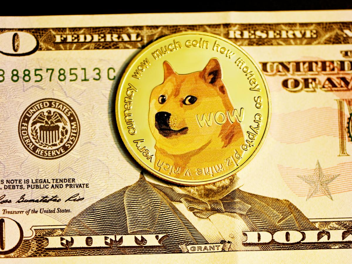 A gold coin with the DOGE dog on it, lies over the face on a $50 bill.
