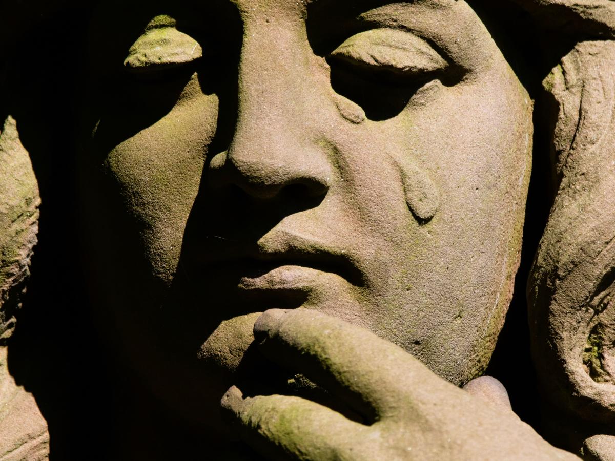 A stone statue's face depicts a falling tear.