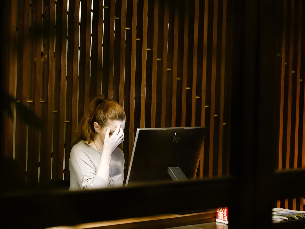 A woman rubs her face in worry, while siting at a screen.