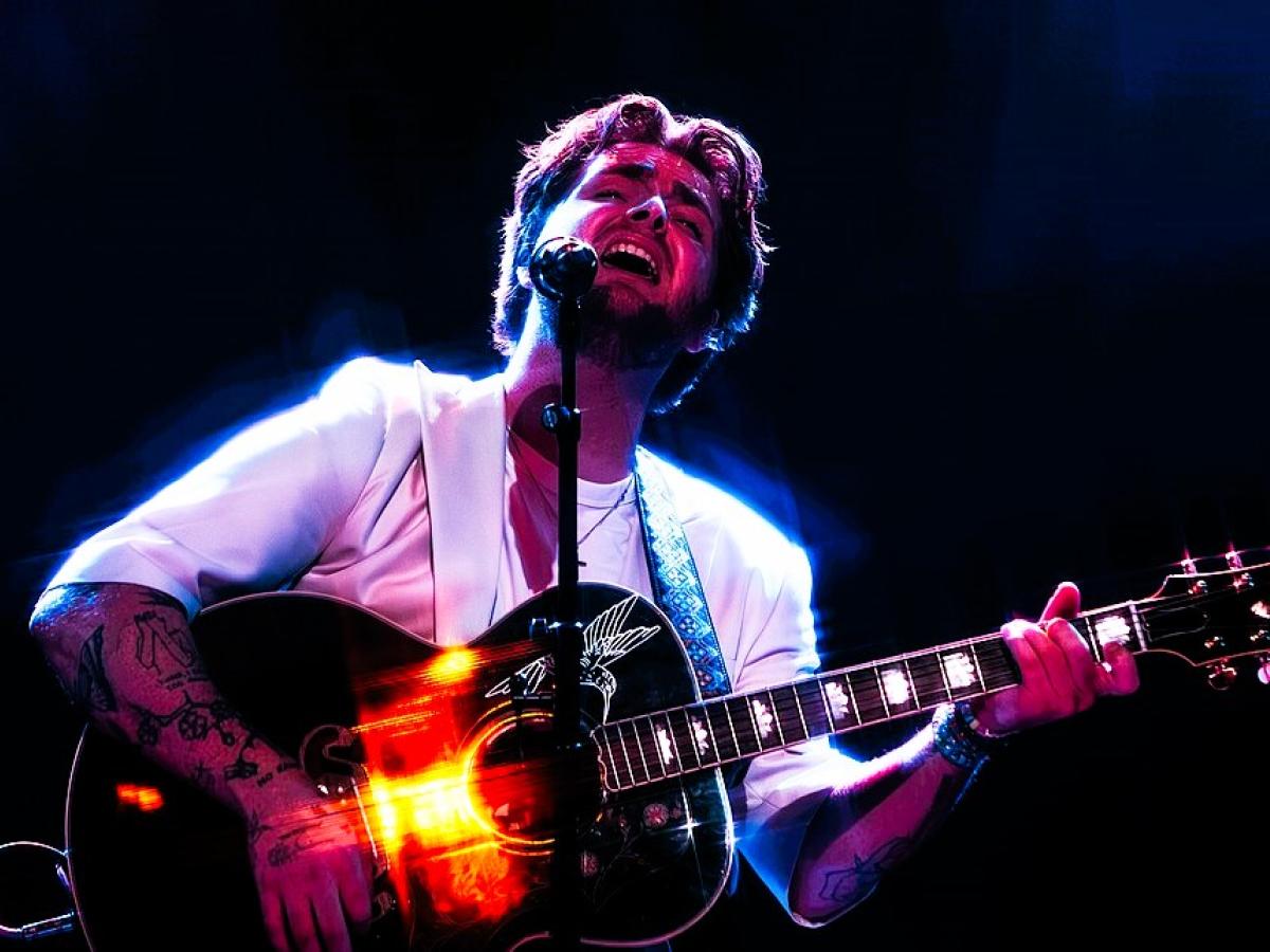 A singer holding a guitar raises his head with closed eyes.