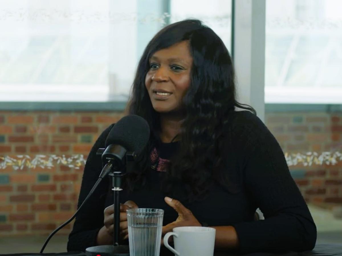 A podcast guest sits in front of a mic talking and gesturing with her hands.