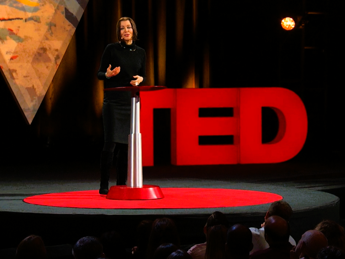 A speaker stands beside a podium in front of a TED sign.