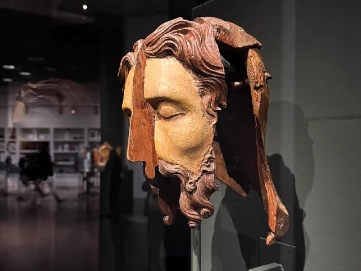 A split wooden sculpted head stands in an exhibition.