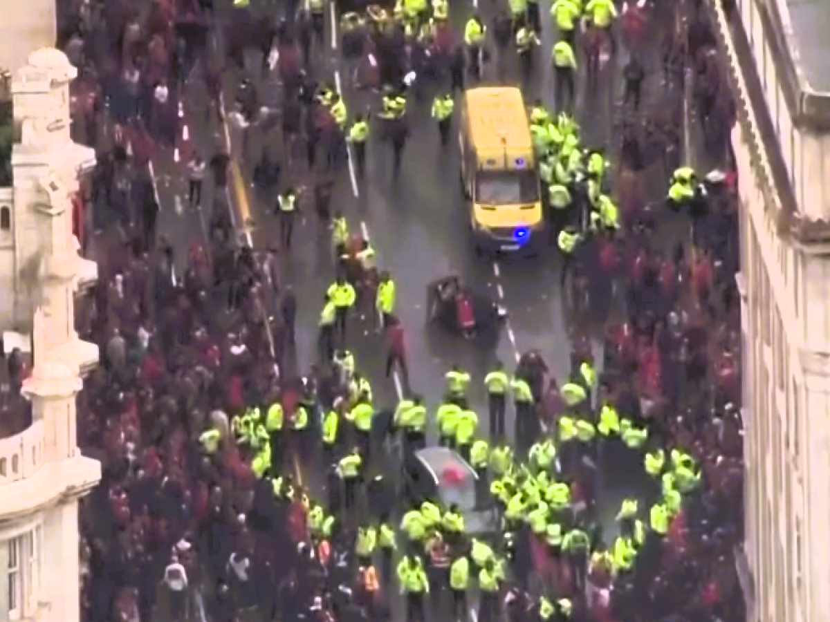 Aerial view of a yellow-jacketed police forming a cordon within a crowd.