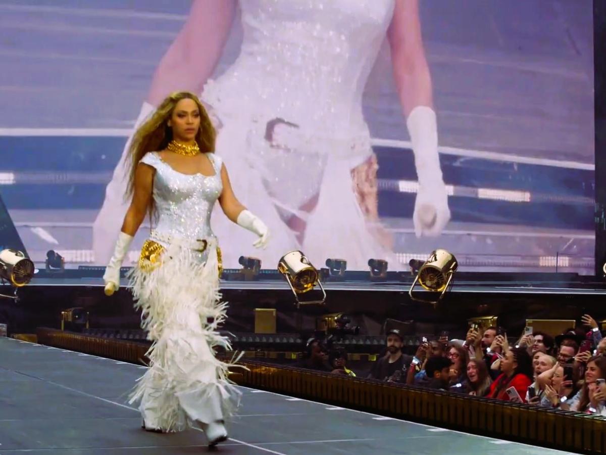 Beyonce marches along a stage catwalk as photographers stare from below.