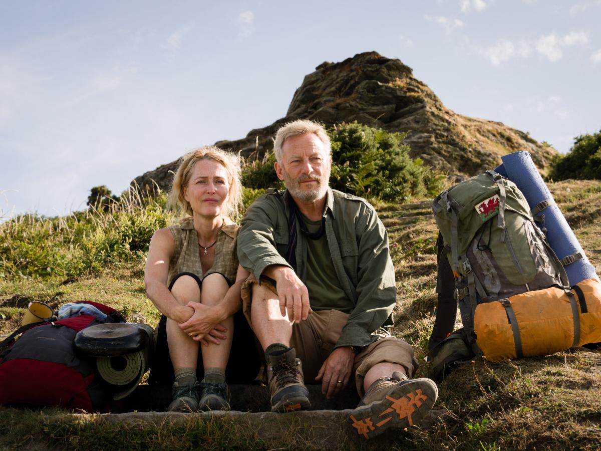 A hiking couple sit on the grass next to a pack.