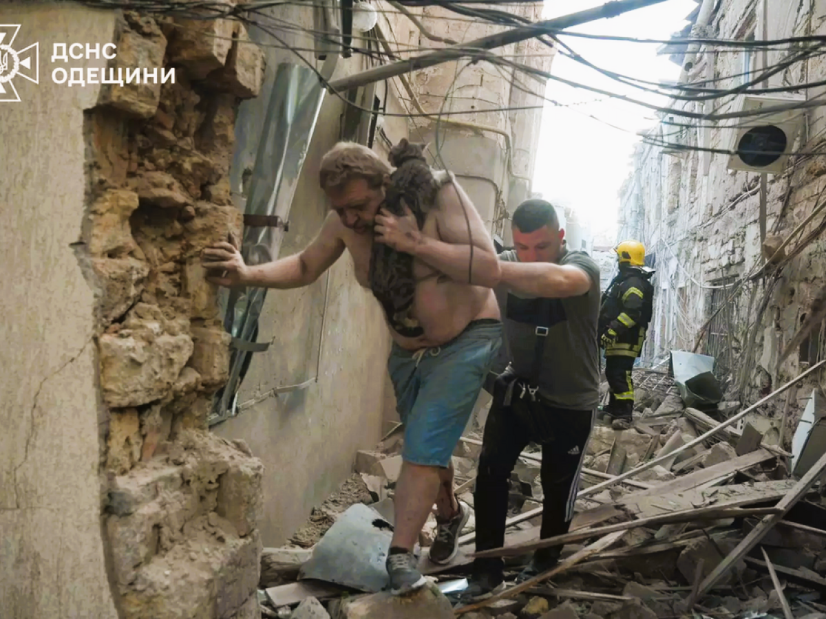 Amid a bombed alley, a victim is helped to walk by a rescue worker