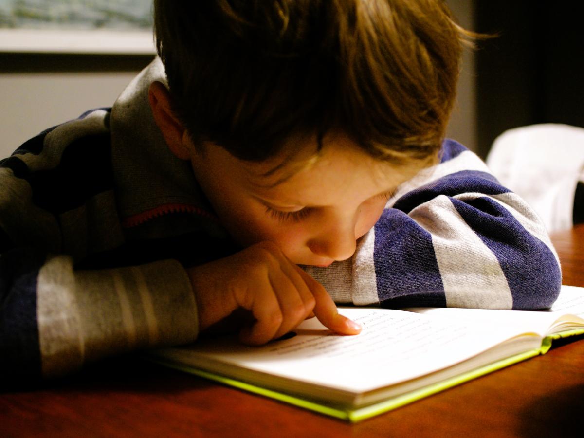 A young boy pores over a book tracing the lines with a finger.