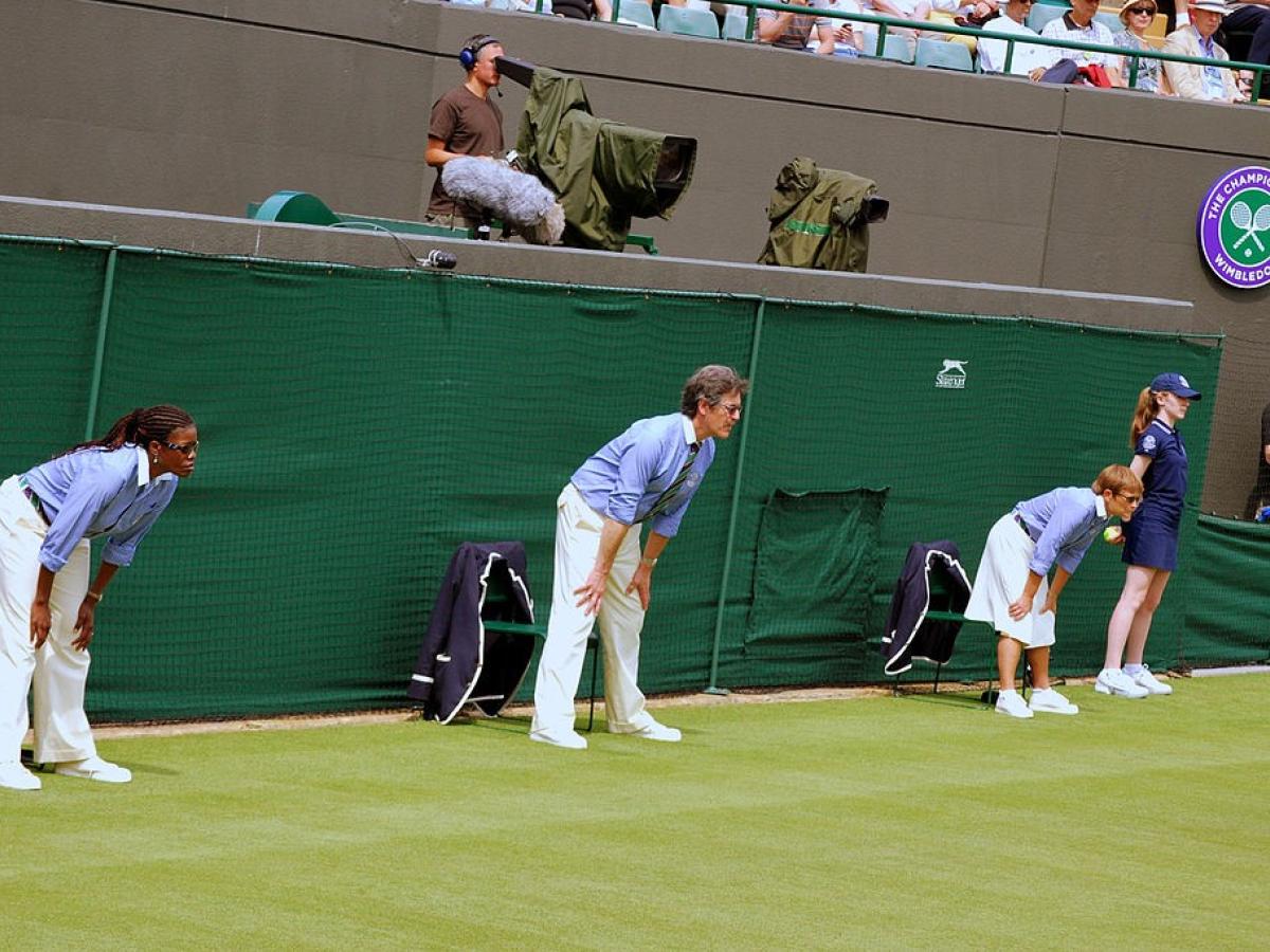 Tennis line judges stand and lean forward with hands on knees