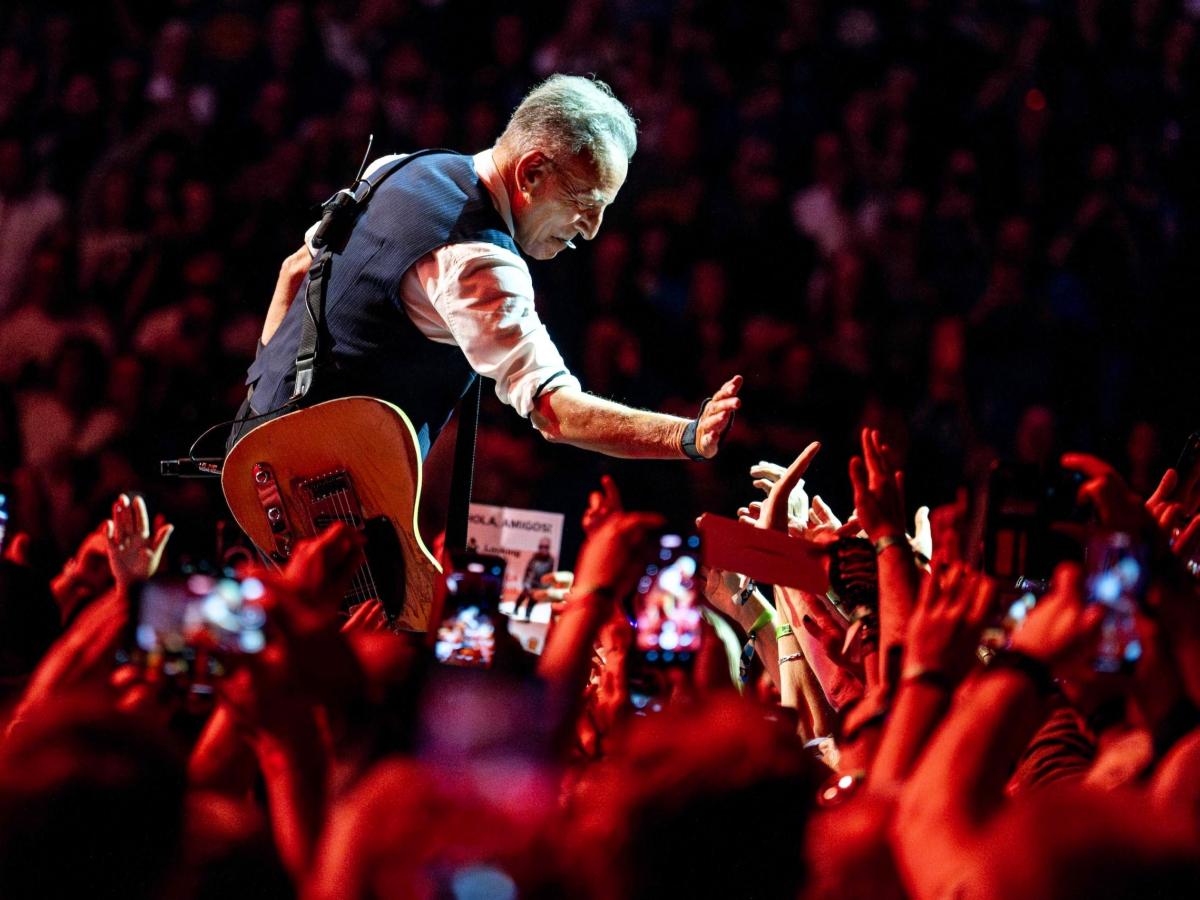 Bruce Springsteen crouches down and holds a hand out to a sea of outstretched hands