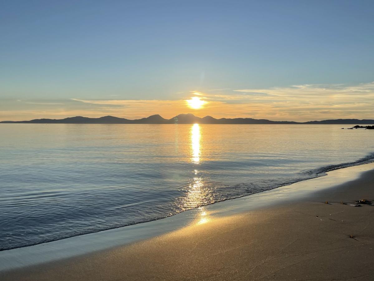 A sunset over an island casts golden light on the sea and a beach.