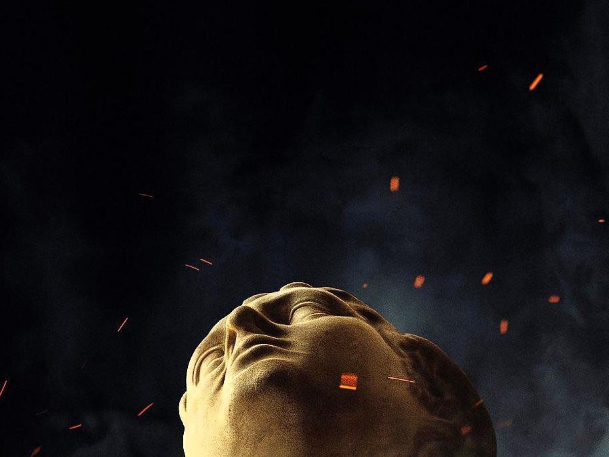 the head of a classical statue looks up amid embers around it.