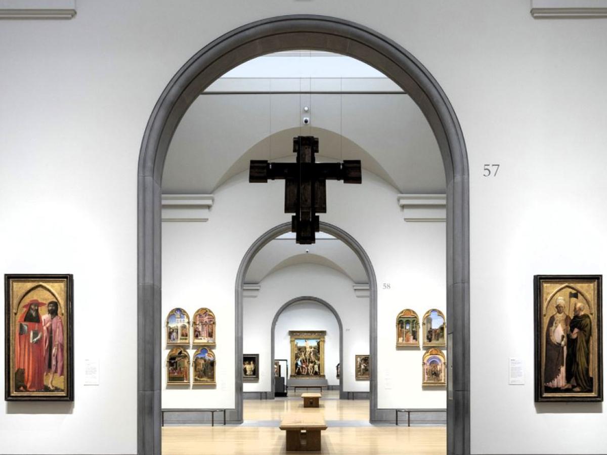 An art gallery arch reveals a suspended crucifix and other paintings in a distant room