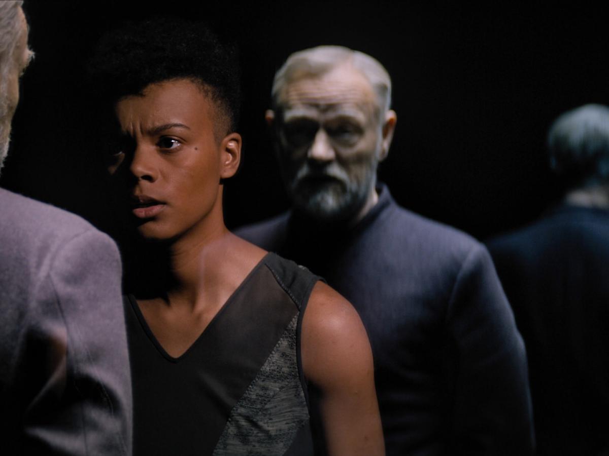 A woman confronts a man whose clone stands behind her.