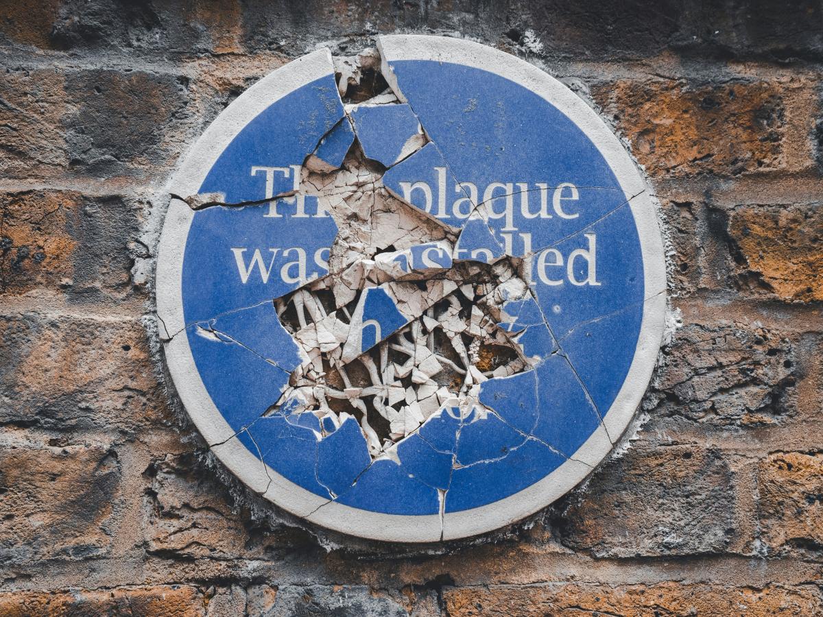 A commemorative blue plaque on a a wall is smashed to pieces