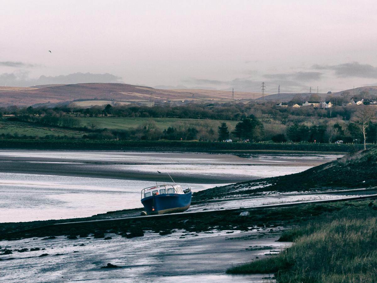 A boat rests on a mud bank of a river, hills are in the background.