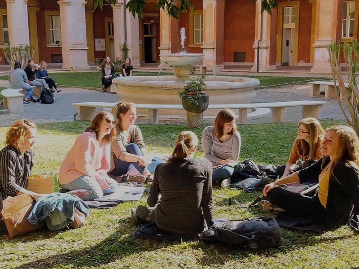 Students sit on the grass in front of a fountain.