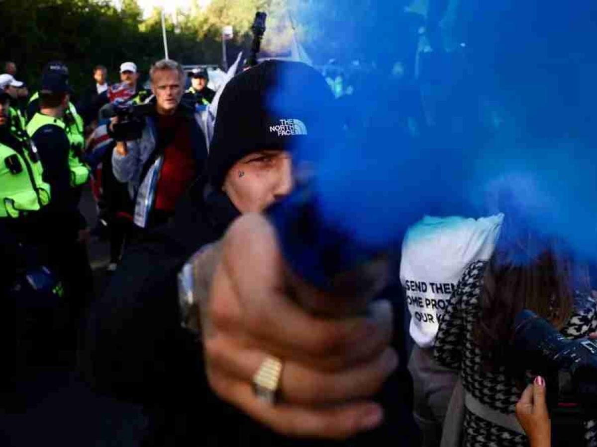 A protestor holds a blue smoke canister towards the camera lens.