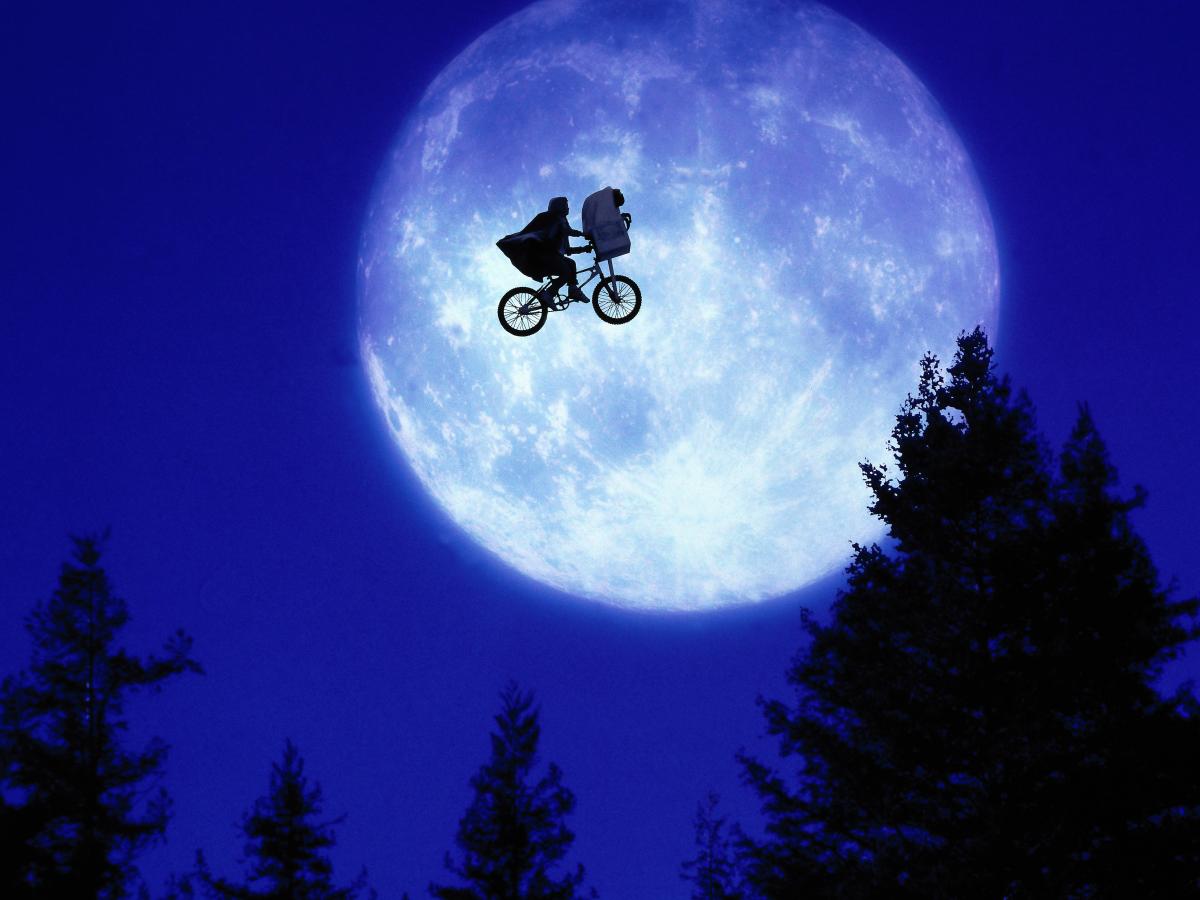 A child and E.T. ride a BMX bike across a moon lit sky.