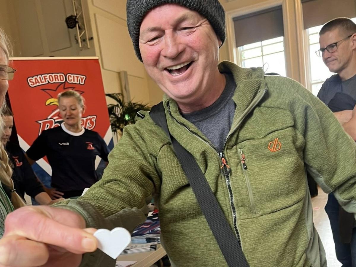 A man presents a heart shaped paper token towards the camera
