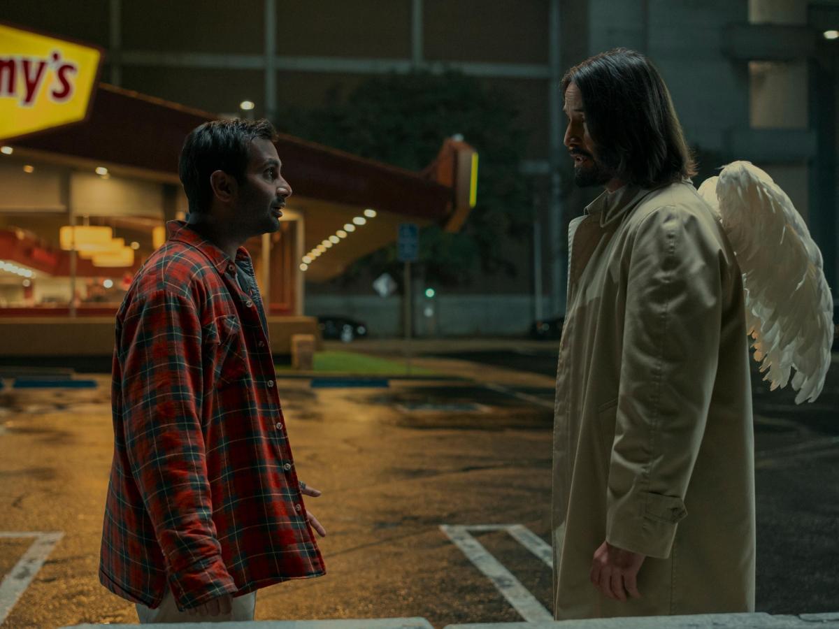 A film character talks to an angel in the street who has wings on the back of his coat.