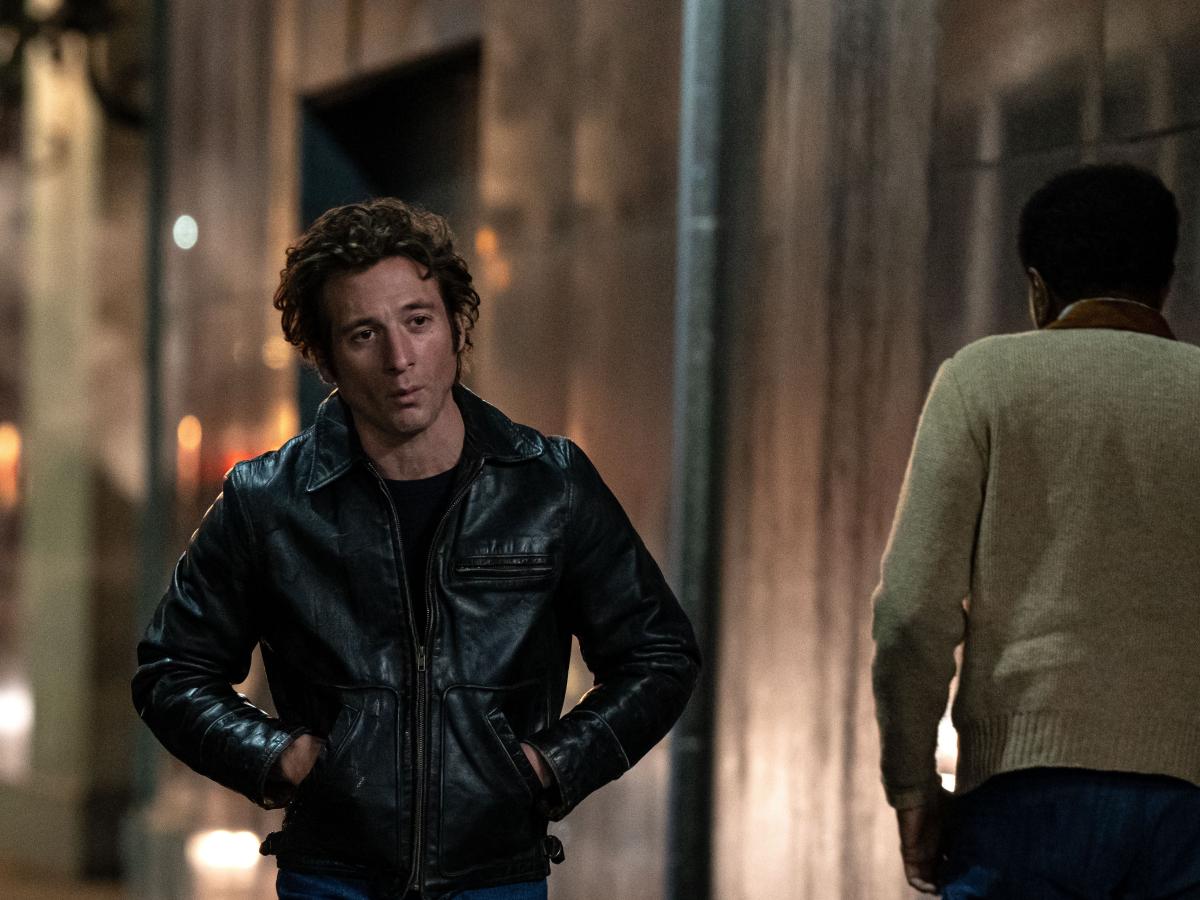 An actor playing Bruce Springsteen walks down a dark street, hands in jacket pocket.