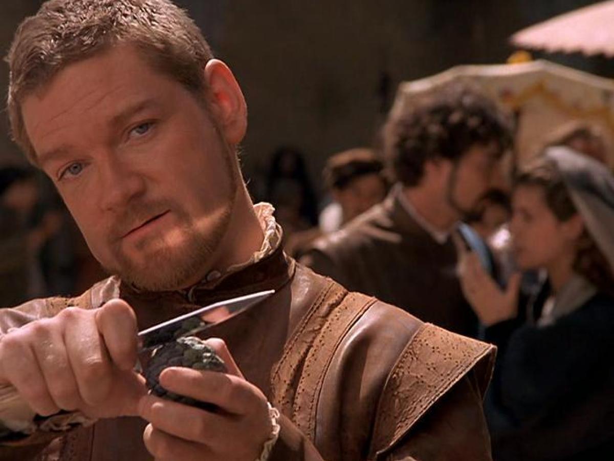 An Elizabethan man holds a dagger up while grinning.