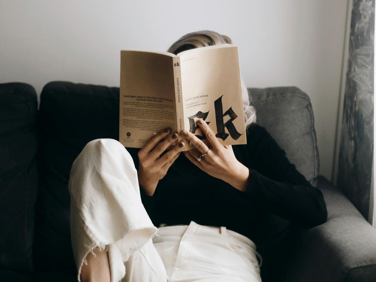   A reader sits on a sofa with a raised leg and holds a book