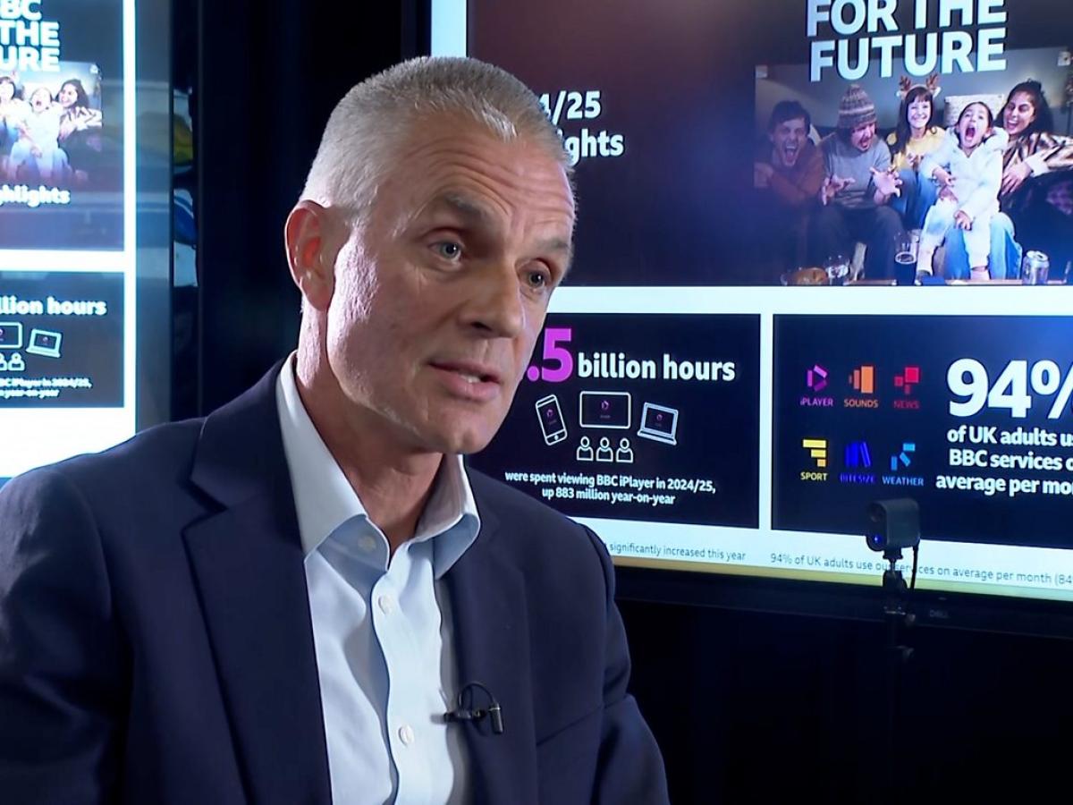 TIm Davie, sits in an interview in front of screens showing facts about the BBC