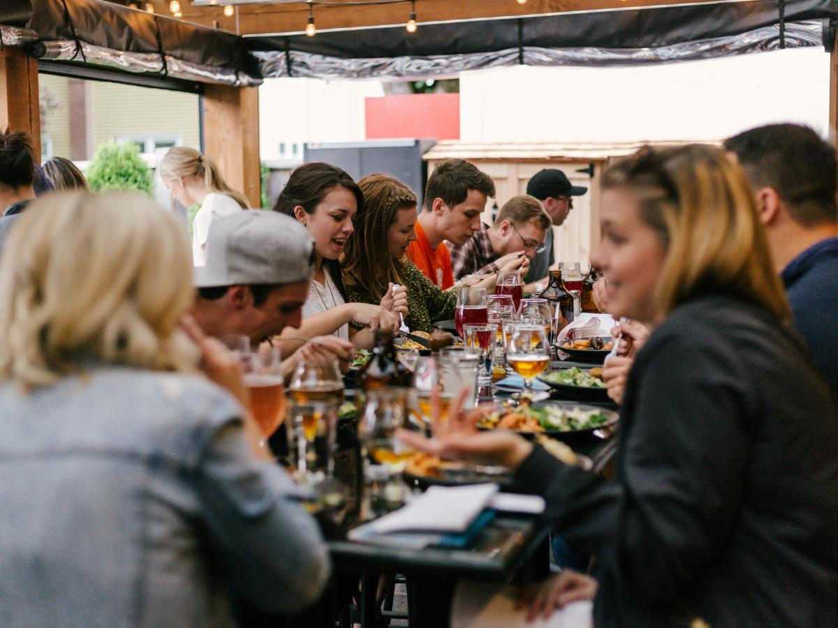 A group of friends sit arouns a large table eating together.