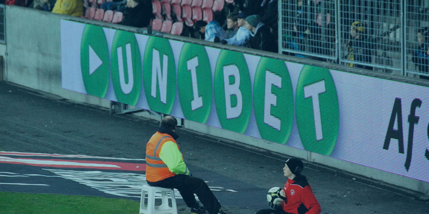 The edge of a football pitch showing an advertising hoarding with a betting brand name on it.