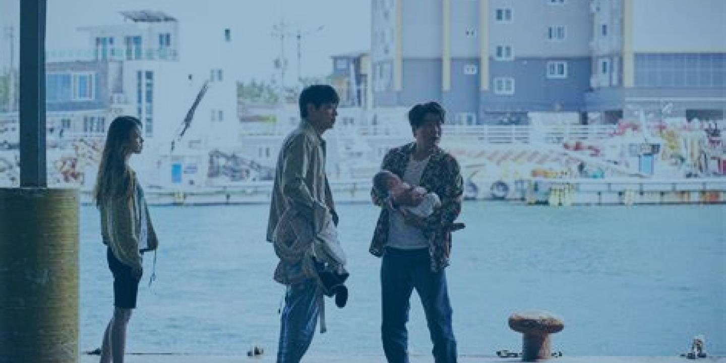 Three people, one carrying a baby, stand on a dock side at a harbour