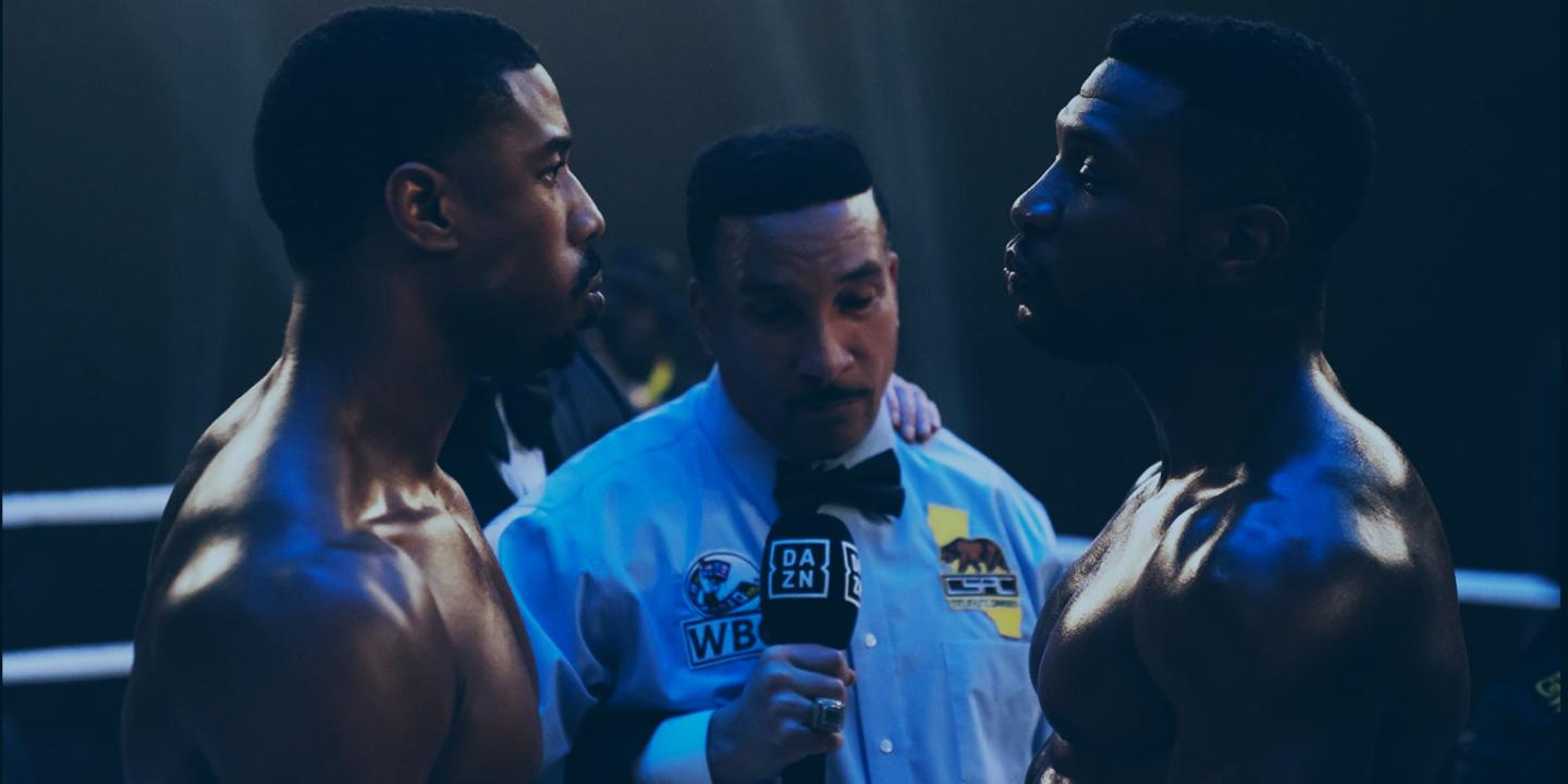 In a boxing ring, an umpire stands between two boxers who stare hard at each other.