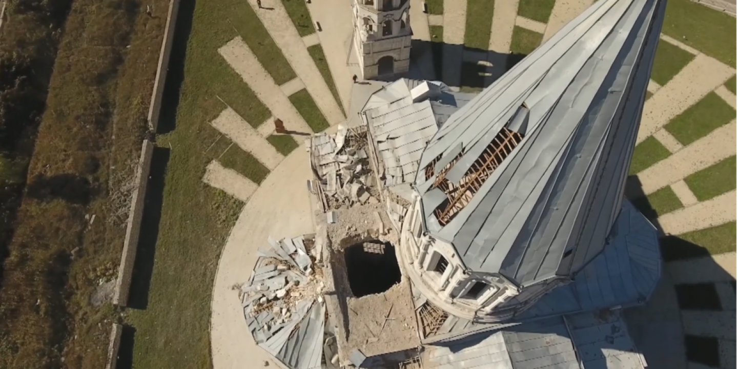An aerial view looking down the damaged spire of a cathederal to a holes in the roof caused by shelling.