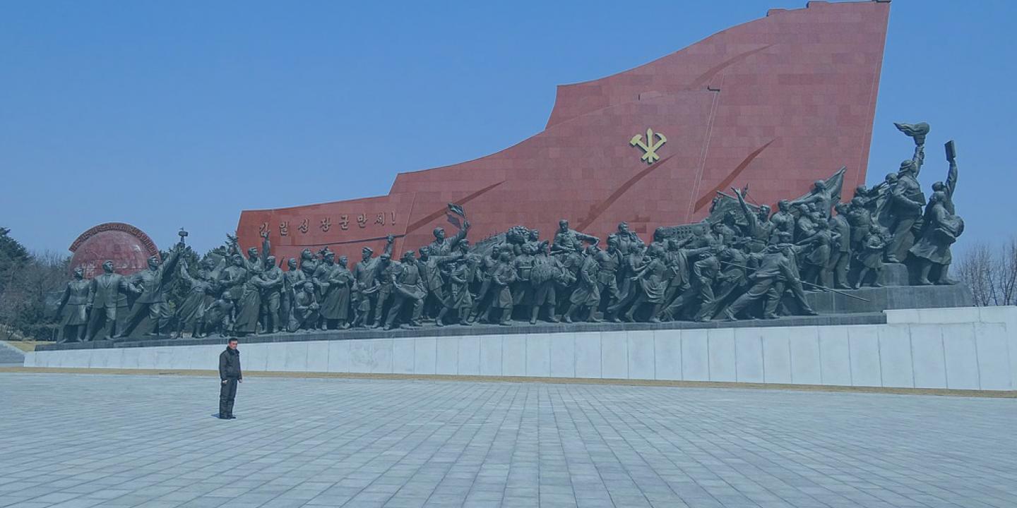 A huge communist monument consists of a red flag wall rising from left to right over a column of statues.